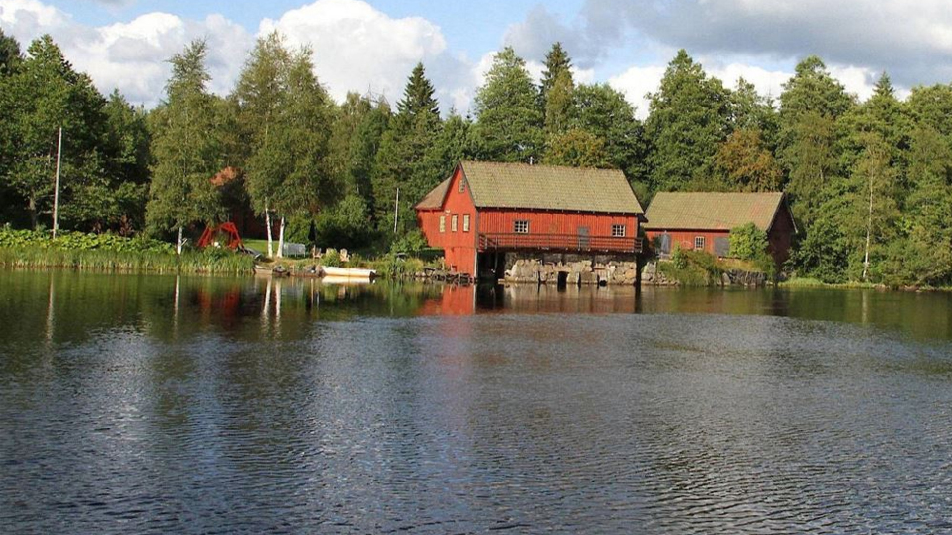 Röda ladugårdsbyggnader fotade från vattnet.