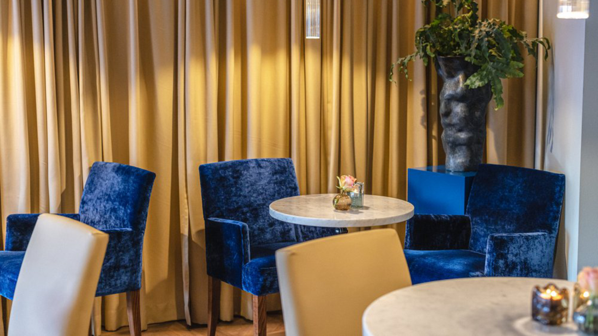 Blå sammetsbeklädda stolar, runda bord, interiört café.