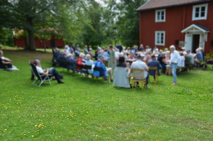 Människor på stolar framför en röd stuga.